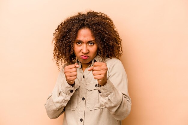 Foto jovem afro-americana isolada em fundo bege mostrando punho para câmera expressão facial agressiva