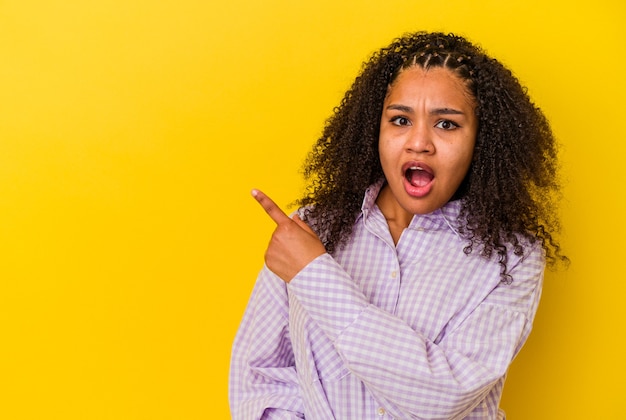 Jovem afro-americana isolada em um fundo amarelo apontando para o lado