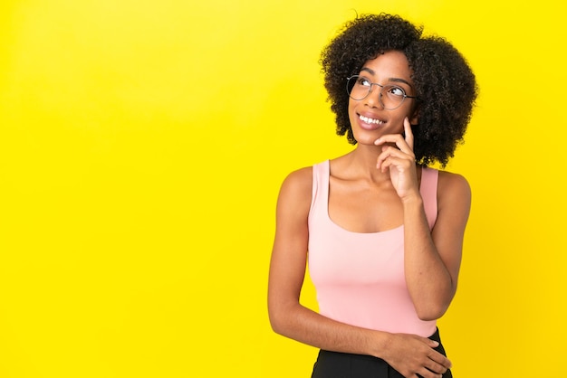 Jovem afro-americana isolada em um fundo amarelo pensando em uma ideia enquanto olha para cima