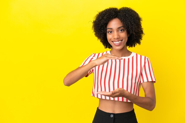 Jovem afro-americana isolada em um fundo amarelo segurando copyspace imaginário na palma da mão para inserir um anúncio