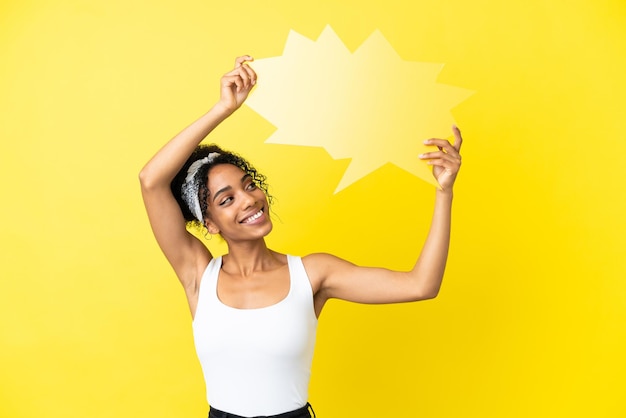 Jovem afro-americana isolada em um fundo amarelo segurando um balão vazio.