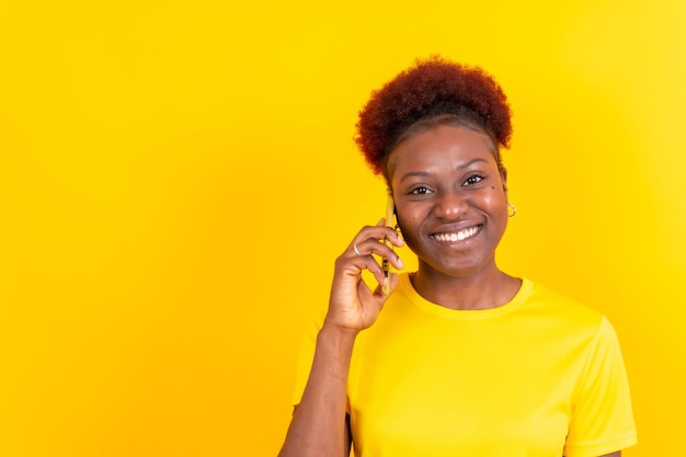 Foto jovem afro-americana isolada em um fundo amarelo sorrindo com a sessão de estudo do celular