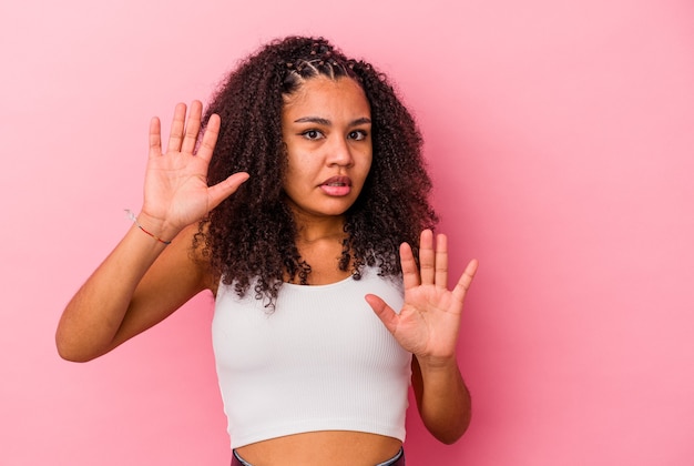 Jovem afro-americana isolada em um fundo rosa, chocada devido a um perigo iminente