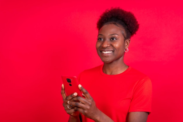 Jovem afro-americana isolada em um fundo vermelho sorrindo com a sessão de estudo do celular