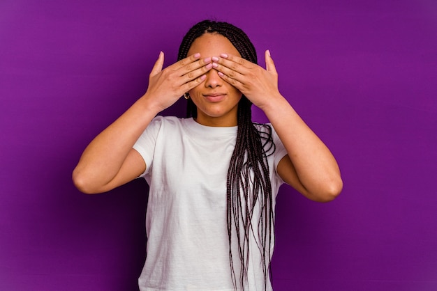 Jovem afro-americana isolada na parede amarela com medo de cobrir os olhos com as mãos