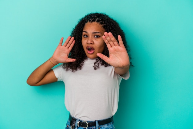 Jovem afro-americana isolada na parede azul, chocada devido a um perigo iminente