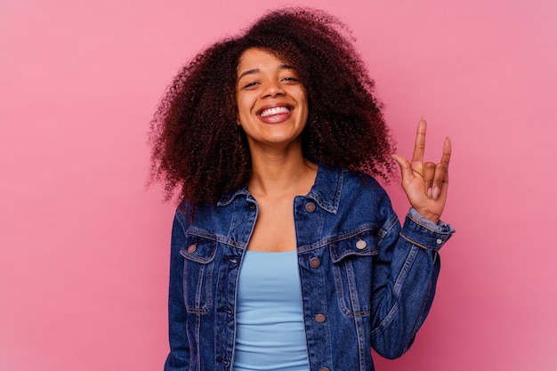 Jovem afro-americana isolada na rosa mostrando um gesto de pedra com os dedos