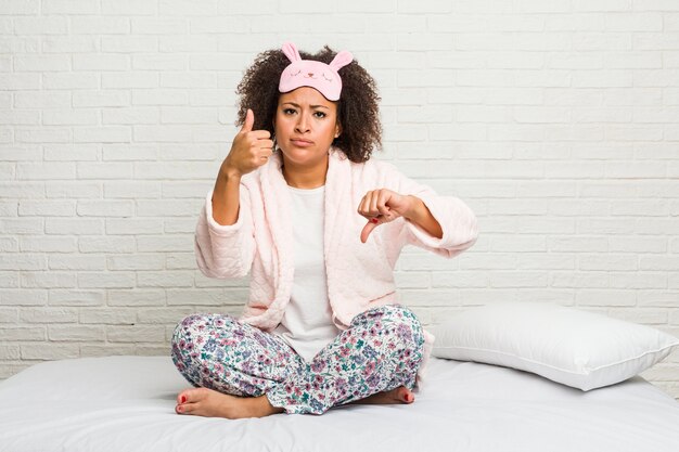 Jovem afro-americana na cama com pijama mostrando os polegares para cima e para baixo