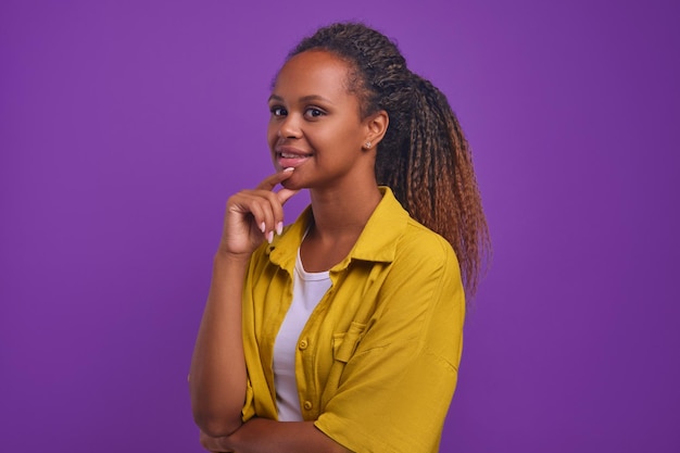 Jovem afro-americana otimista toca o queixo em pose pensativa