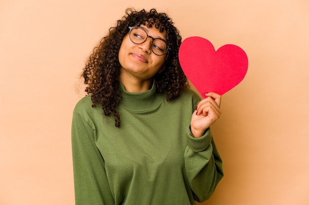 Foto jovem afro-americana segurando um coração de dia dos namorados, sonhando em alcançar objetivos e propósitos