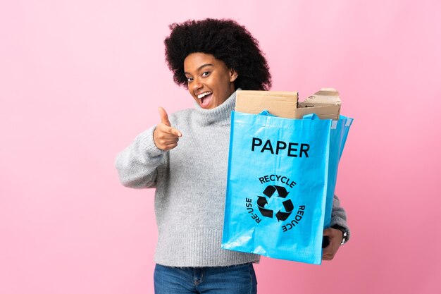 Jovem afro-americana segurando uma sacola reciclada isolada em colorido apontando para a frente e sorrindo