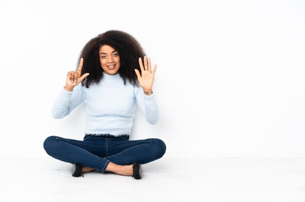 Jovem afro-americana sentada no chão contando sete com os dedos