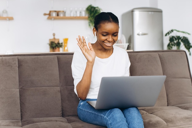 Jovem afro-americana trabalhando no laptop sentado no sofá na cozinha