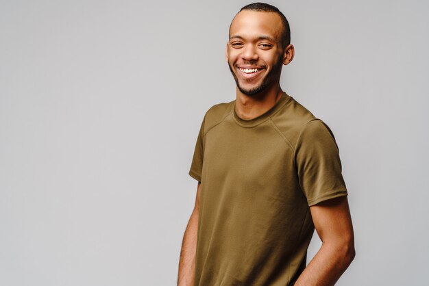 Foto jovem afro-americano alegre e amigável com uma camiseta verde sobre uma parede cinza claro