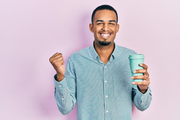 Jovem afro-americano bebendo uma xícara de café para viagem gritando orgulhoso comemorando a vitória e o sucesso muito animado com o braço erguido