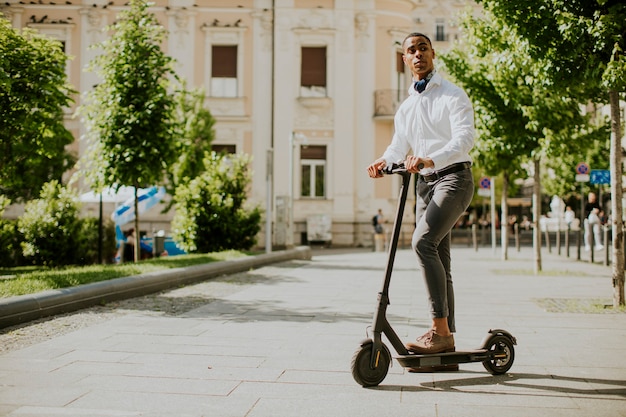 Jovem afro-americano bonito usando scooter elétrico em uma rua