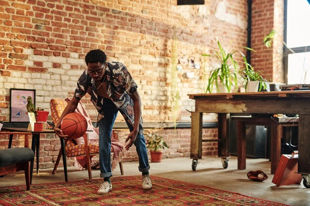 Jovem afro-americano com bola jogando no tapete na sala de estar