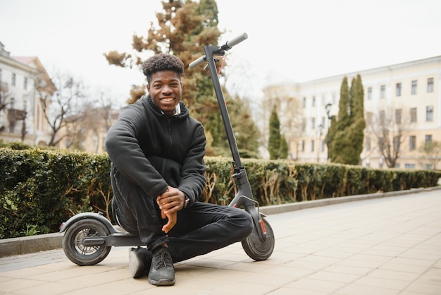 Jovem afro-americano com scooter elétrico na cidade