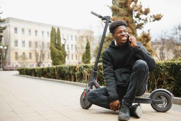 Jovem afro-americano com scooter elétrico na cidade