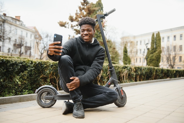 Jovem afro-americano com scooter elétrico na cidade