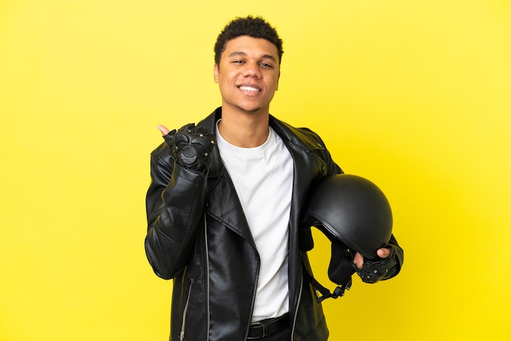 Foto jovem afro-americano com um capacete de motociclista isolado em um fundo amarelo apontando para o lado para apresentar um produto