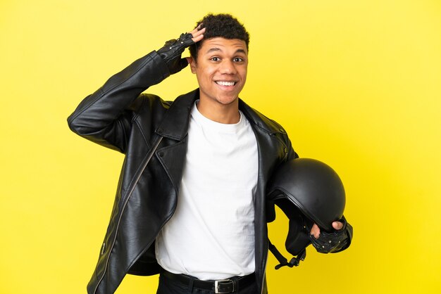 Jovem afro-americano com um capacete de motociclista isolado em um fundo amarelo com expressão de surpresa