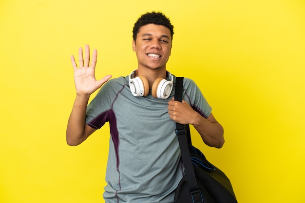 Jovem afro-americano com uma bolsa esportiva isolada em um fundo amarelo, contando cinco com os dedos