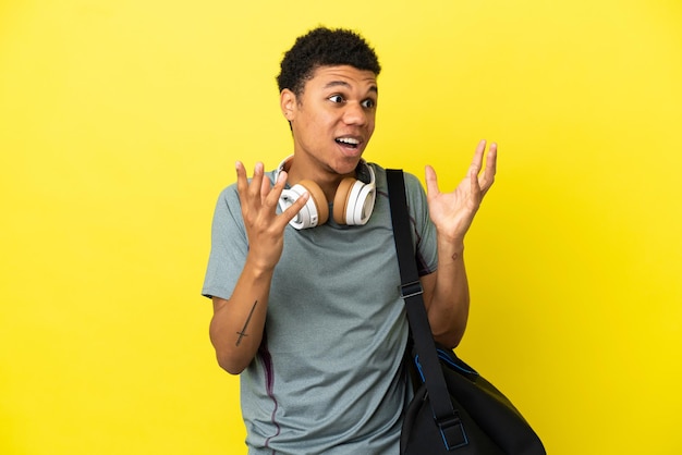 Jovem afro-americano com uma bolsa esportiva isolada em um fundo amarelo e uma expressão facial surpresa