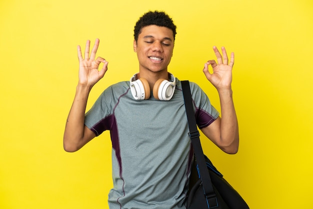 Jovem afro-americano com uma bolsa esportiva isolada em um fundo amarelo em pose zen