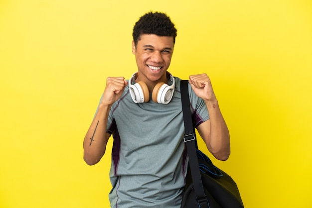 Jovem afro-americano com uma sacola esportiva isolada em um fundo amarelo, comemorando a vitória na posição de vencedor