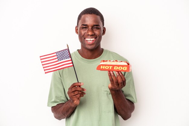 Jovem afro-americano comendo cachorro-quente e segurando a bandeira americana isolada no fundo branco