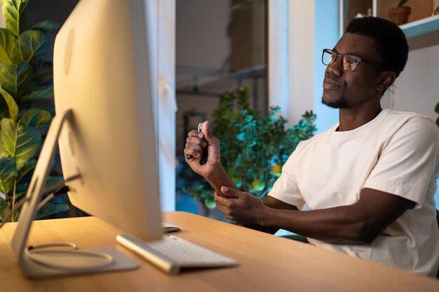 Jovem afro-americano cuida do pulso de mão usando expansor durante muito tempo de trabalho no computador