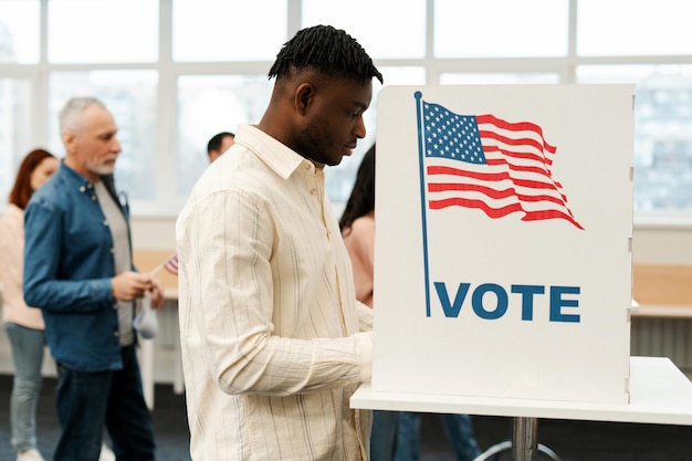 Jovem afro-americano de pé na cabine de votação com a bandeira americana votando na estação eleitoral