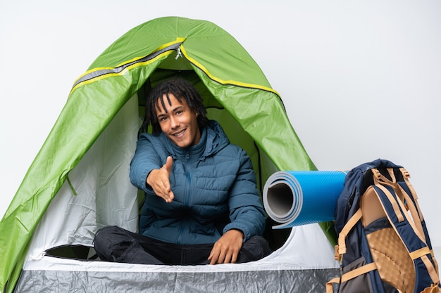 Jovem afro-americano dentro de uma barraca de acampamento verde, apertando as mãos para fechar um bom negócio