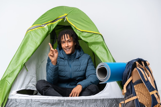 Jovem afro-americano dentro de uma barraca de acampamento verde, apontando o dedo para o lado