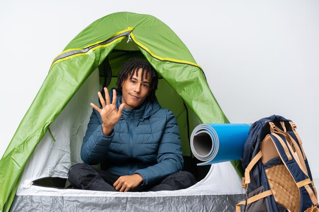 Jovem afro-americano dentro de uma barraca de acampamento verde, contando cinco com os dedos