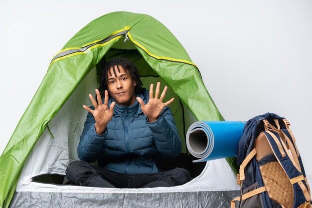 Foto jovem afro-americano dentro de uma barraca de acampamento verde contando dez com os dedos