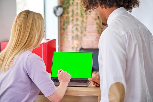 Jovem afro-americano e jovem loira em um escritório com tela verde de croma de laptop