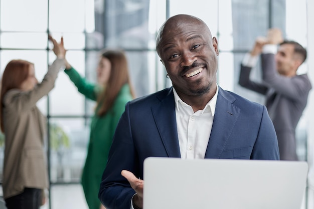 Jovem afro-americano em terno de negócios segurando laptop em pé no corredor do escritório