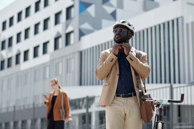 Jovem afro-americano em traje de luxo tranquilo, apertando o cinto do capacete de segurança