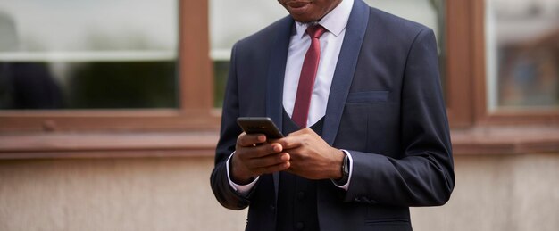 jovem afro-americano em uma jaqueta azul e gravata vermelha segura um telefone celular em suas mãos closeup