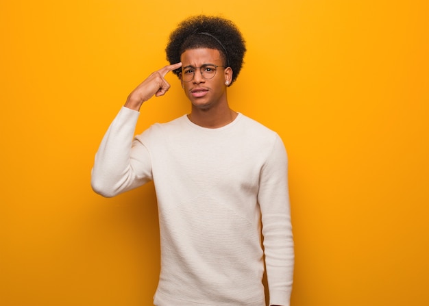 Jovem afro-americano em uma parede laranja fazendo um gesto de decepção com o dedo