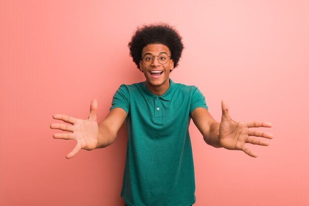 Jovem afro-americano em uma parede rosa muito feliz dando um abraço na frente