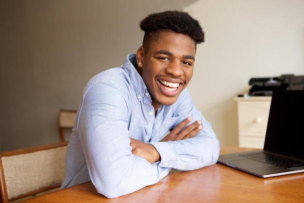 jovem afro-americano encantador sentado em uma mesa com um computador portátil