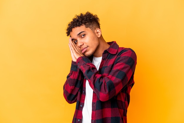 Jovem afro-americano encaracolado amarelo bocejando, mostrando um gesto cansado, cobrindo a boca com a mão.