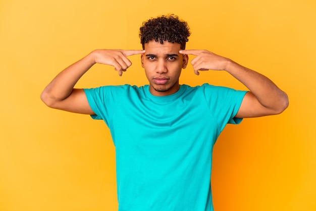 Jovem afro-americano encaracolado isolado em roxo focado em uma tarefa, mantendo os indicadores apontando a cabeça.