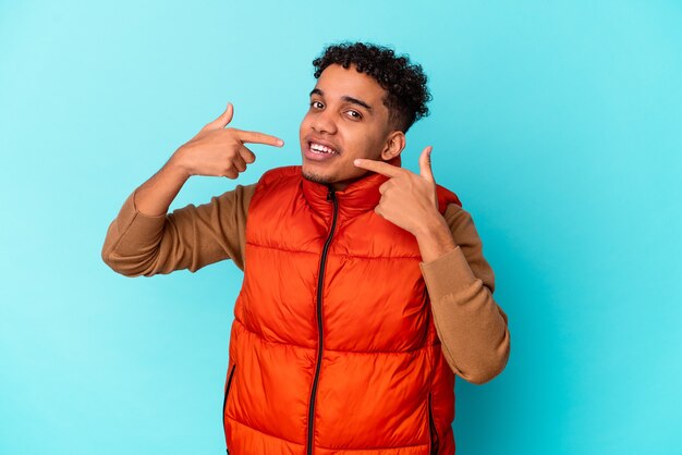 Jovem afro-americano encaracolado isolado em sorrisos azuis, apontando o dedo para a boca.