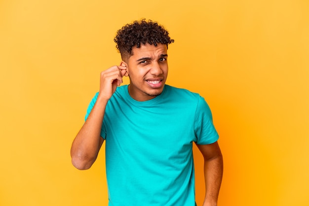 Jovem afro-americano encaracolado isolado no roxo, cobrindo as orelhas com as mãos.