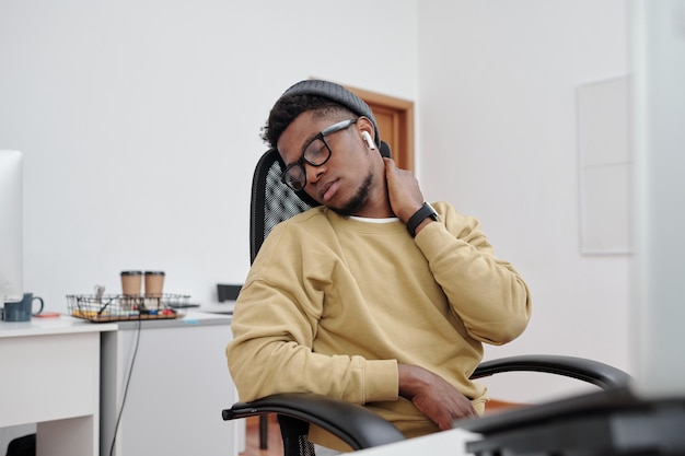 Jovem afro-americano fazendo exercícios relaxantes para o pescoço em seu local de trabalho