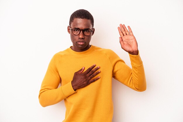 Jovem afro-americano isolado em fundo branco fazendo um juramento colocando a mão no peito